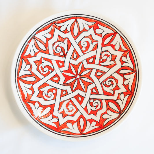 Assiette en céramique blanche marocaine peinte à la main, éclatante en rouge et blanc avec une bordure noire, reflétant une atmosphère d'authenticité.